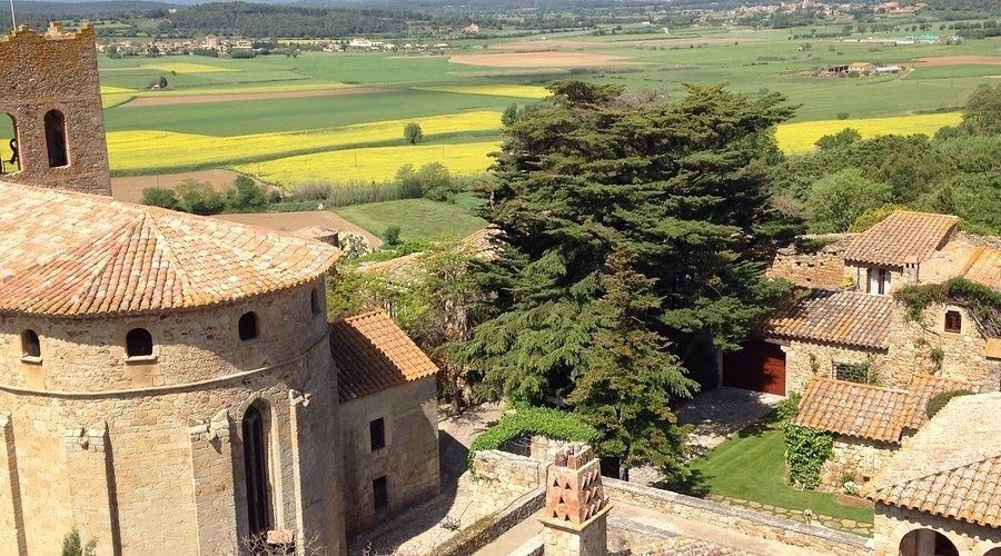 Historische Steinkirche mit Ziegeldächern über gelben Feldern in Katalonien